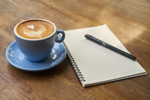 photo of cup of coffee, a notepad and a pen